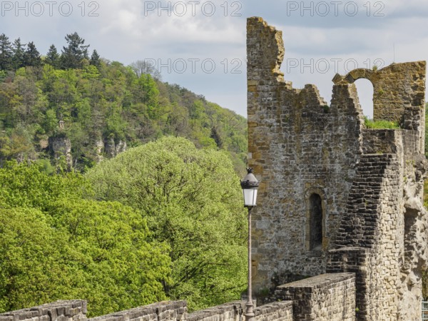 Castle ruins surrounded by a lush forest, old stone tower with wall and lantern in the foreground, Luxembourg