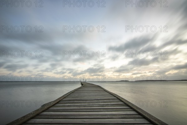 Sunrise over a lake in autumn. A wooden jetty juts into the water, while grass has established itself on the sandy beach. The lake and beach at Lake Vänern in Näs Sannar, Sweden, Scandinavia