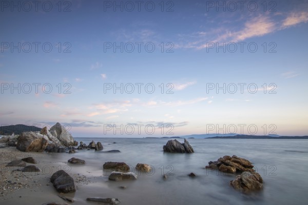 View through rocks on a sandy beach into the sunset. Landscape shot with view to the horizon over the wide sea at the coast of Ouranoupoli, Thessaloniki, Central Macedonia, Greece