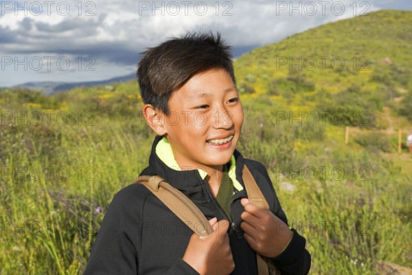 Young sporty Asian boy enjoying and hiking the mountain during the California Golden Poppy and Goldfields blooming in Walker Canyon, California. USA. Asian kid making his way through the mountain