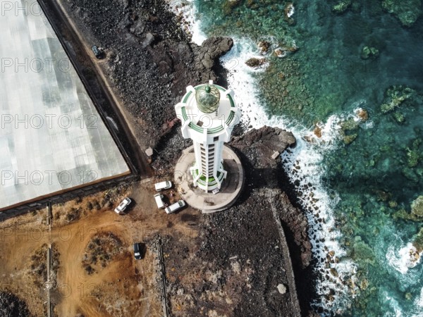 Aerial top view of lighthouse, rocks and ocean waves in a volcanic landscape with lava. Punta Lava Lighthouse in La Palma. La Bombilla, Tazacorte, Canary Islands. Top aerial view with drone
