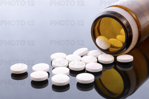 White pills and brown glass bottle isolated on black reflective surface. Global pharmaceutical industry for billions dollars per year. Pharmaceutical drugs for use as medications. Studio shot