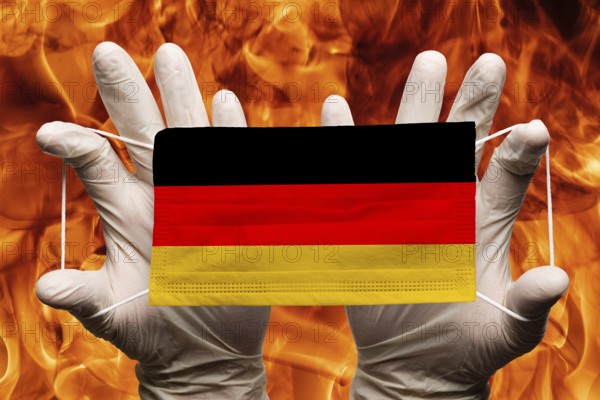 Doctor holding in white gloves protection medical face mask, respiratory bandage with Germany national country flag superimposed on mask. Concept on background of dangerous red flames natural fire