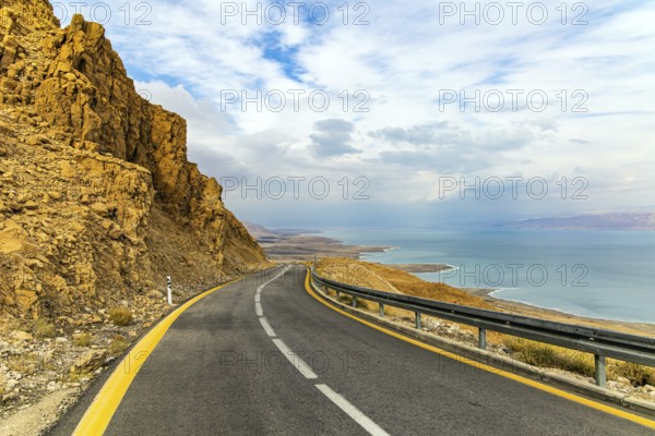 Israel. The highway runs along the coast of the Dead Sea. Jordan on the opposite coast of the sea is illuminated by the dim winter sun. Cloudy January day. The sea surface reflects the clouds