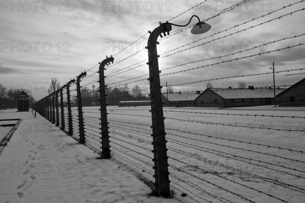 A black and white shot of the outer barbed-wire fence and huts under snow in winter at the Auschwitz-Birkenau concentration camp. Birkenau, Poland