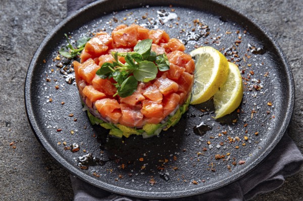 Food, Raw salmon, avocado purple onion salad served in culinary ring on black plate. Black concrete background
