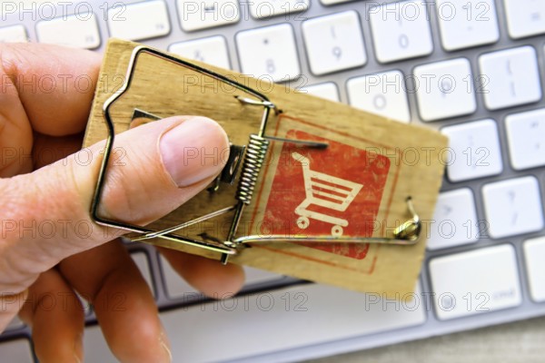 Hand in mousetrap with shopping trolley in front of a computer keyboard, photomontage