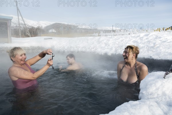 KAMCHATKA PENINSULA, RUSSIA, FEB 02, 2013: Two joyful women photographed while swimming in geothermal spa in hot spring pool in winter. Eurasia, Russian Far East, Kamchatsky Krai, Anavgay Village