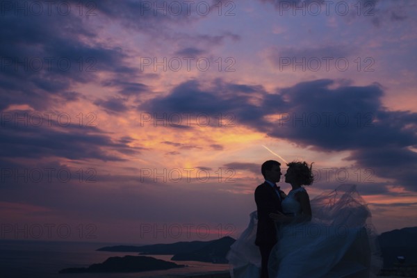 Silhouette of the newlyweds against the sky at sunset. Wedding in Montenegro. Silhouette of a couple. Silhouette of the bride and groom