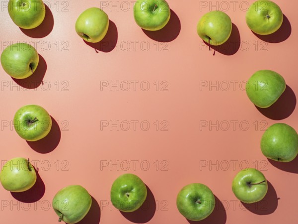 Green apples on orange or coral pink background with copy space for text or design in center, Colorful fruit frame. Flat lay or top view, Hard light