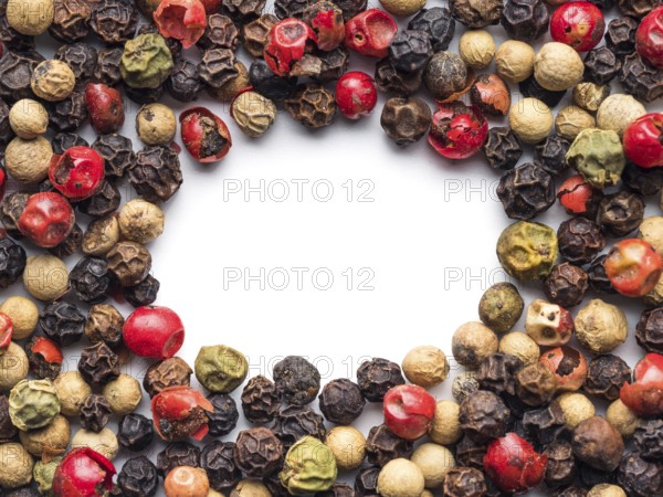Mixed peppercorns background with white copy space in center. Food background with peppercorns. Different colored peppercorns pattern on white background, top view or flat lay