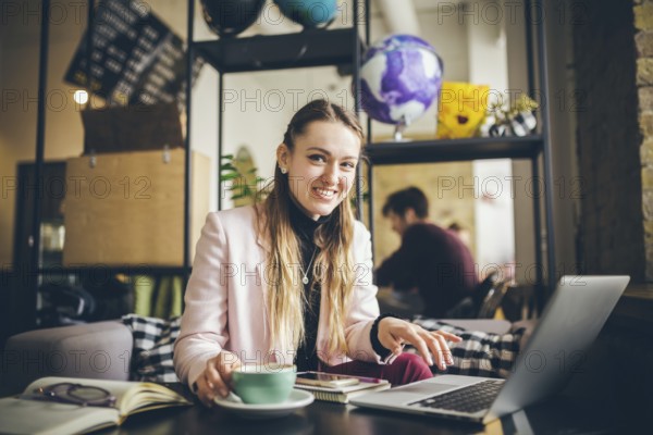 Beautiful young caucasian woman drinking coffee and typing on a keyboard inside a cafe at a wooden table. The topic of modern professions is a blogger, freelancer and writer