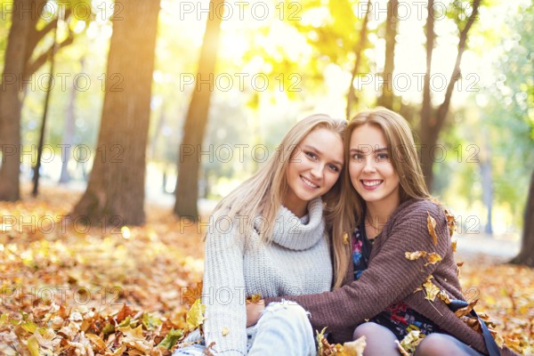 Fashionable beautiful young girlfriends walking together in the autumn park background. Having fun and posing. Toned in retro style