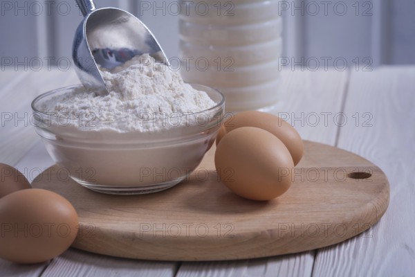 Very close up view eggs flour in bowl scoop bottle of milk on white painted old wooden board food and drink concept