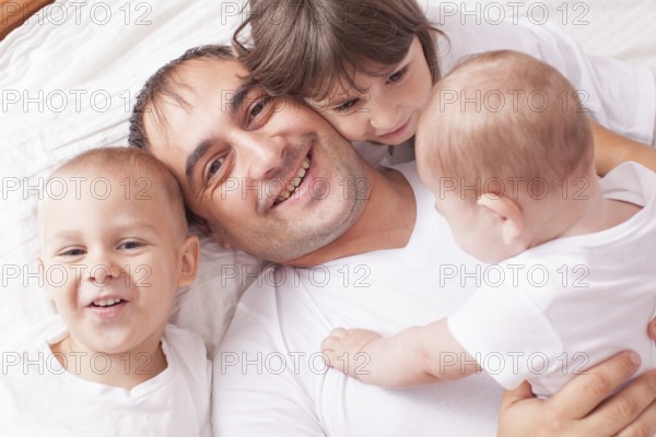 The father with three children in white laughing and playing on the bed