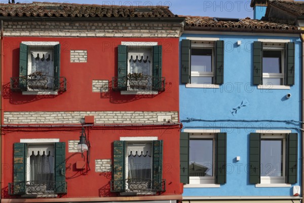 Close-up of red and blue houses with classic shutters and rustic façade, Burano, Venice, Veneto region, Italy