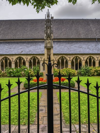 Iron gate in front of a garden in the monastery courtyard with well-tended flowerbeds and Gothic architecture, Xanten, North Rhine-Westphalia, Germany