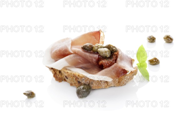 Luxurious canape background. Ciabatta slice with prosciutto, dry tomato and capers isolated on white background. Culinary eating