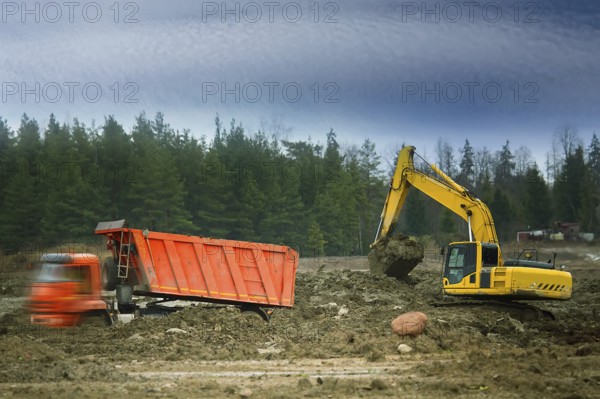 Preparation of the site for construction, leveling the soil. Excavator loads excess soil into blurred dump trucks