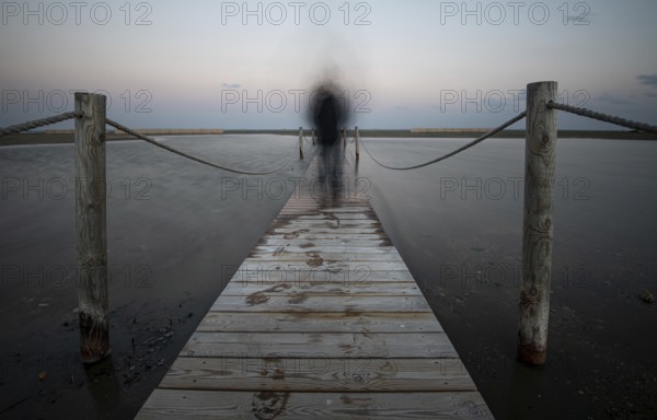 An unrecognised person walking like a ghost at a wooden pier