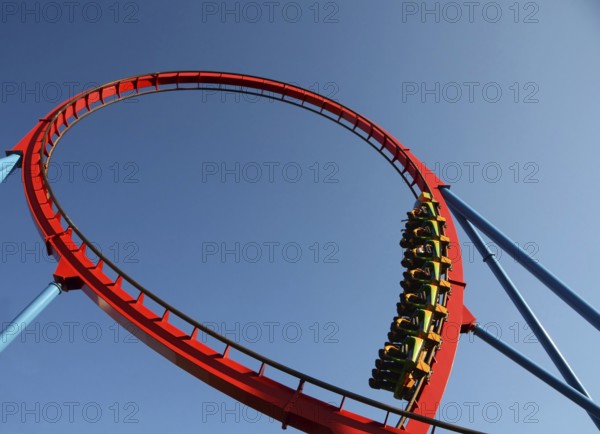 People on a dangerous Rollercoaster Ride in an amusement park against a blue sky