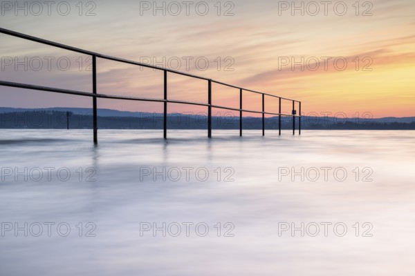 A railing in calm water, surrounded by a pastel-coloured sunrise, lido, Litzelstetten, Lake Constance, Baden-Württemberg, Germany