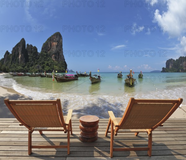 Cozy beach rest. Two wooden chaise lounges and small bedside table on a wooden scaffold. Native boats for sea walks expect tourists near the coast