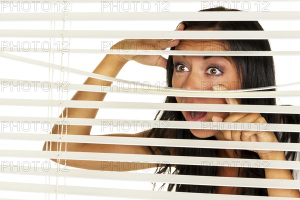 A young woman watches something through the blinds of her window Austria
