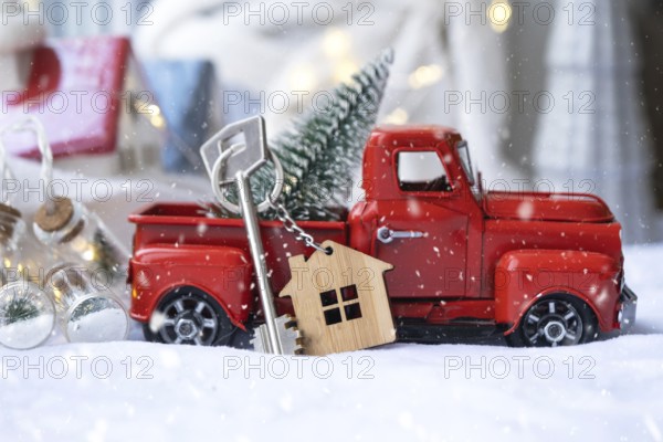 Red retro car with a Christmas tree decorates with the house key in the pickup truck for Christmas. Buying a home, moving, mortgage, loan, real estate, festive mood, New Year