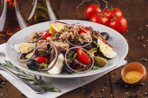 food still-life, Fresh nicoise salad with tuna, eggs, olives, and tomatoes on a wooden table with olive oil and rosemary