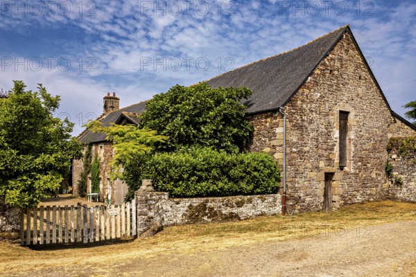 Rural stone house with a small wooden fence and green bushes under a clear sky, The Abbey de La Lucerne in Normandy, France