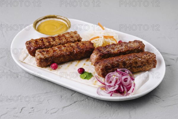 Food, Juicy grilled kebabs served on a white plate with fresh salad and dipping sauce