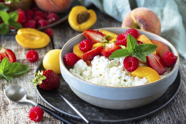 Rustic summer breakfast or dessert. Curd or cottage cheese served with fresh summer fruits and berries on a wooden table