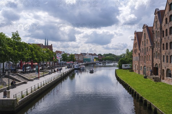 City view with waterway and historic brick buildings, flanked by green areas and clouds, Lübeck, Schleswig-Holstein, Germany