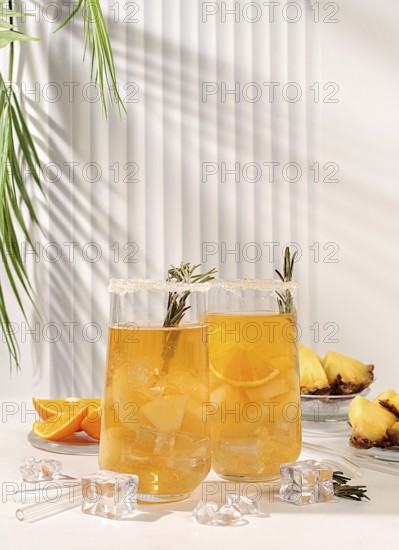 Cold homemade cocktail or lemonade with rosemary, orange, ice and pineapple on a sunny table, Detox diet and summer party concept. Refreshing summer diet drink recipe, restaurant menu, selective approach