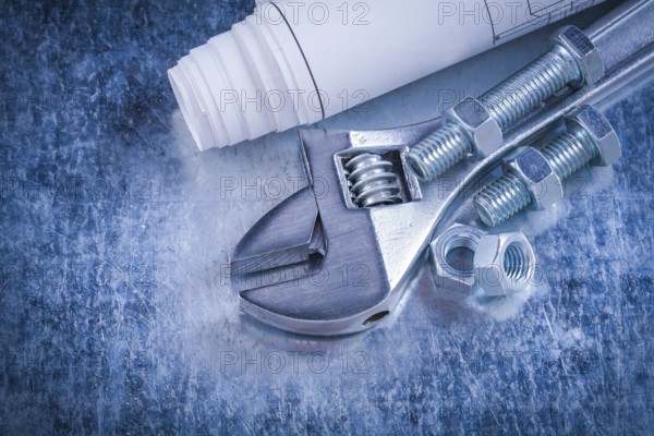 Steel adjustable spanner screw-nuts bolts and blueprints on scratched metallic background construction concept