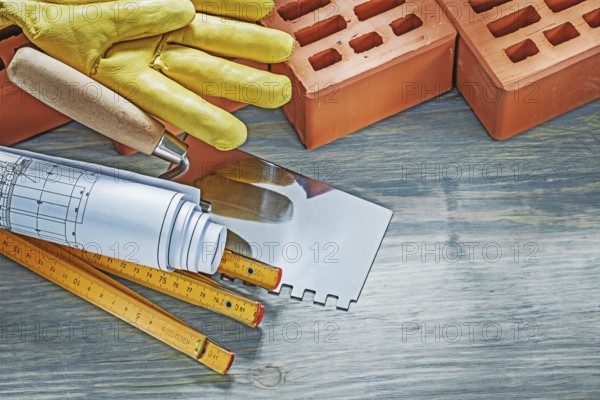 Red bricks working gloves blueprints wooden meter palette plastering trowel on wood board bricklaying concept