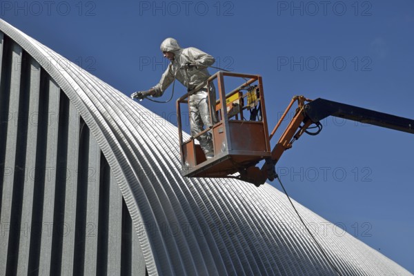 Tradesman spray painting the roof of an industrial building, Greymouth, South Island