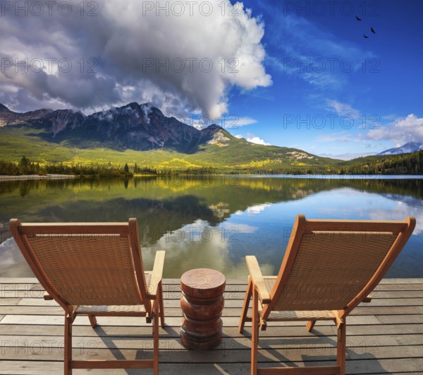 Two comfortable wooden sun beds for tourists, interconnected table. Pyramid Mountain reflected in Pyramid Lake