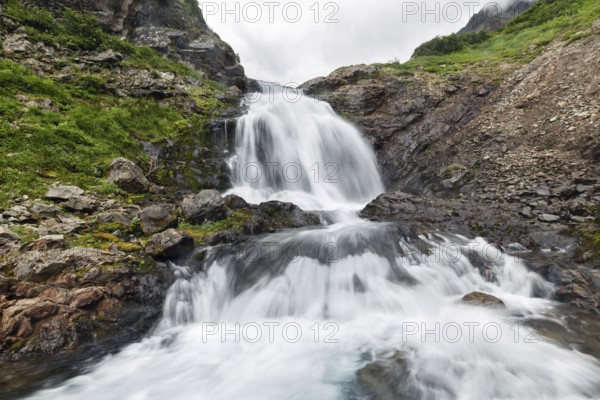Scenery summer mountain landscape of Kamchatka Peninsula: beautiful view of cascade of flowing stormy water in waterfall in Mountain Range Vachkazhets. Eurasia, Russian Far East, Kamchatka Region
