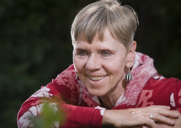 Portrait of an elderly woman on a park bench in summer with her upper body turned backwards over the backrest and looking towards the camera, Berlin, Germany