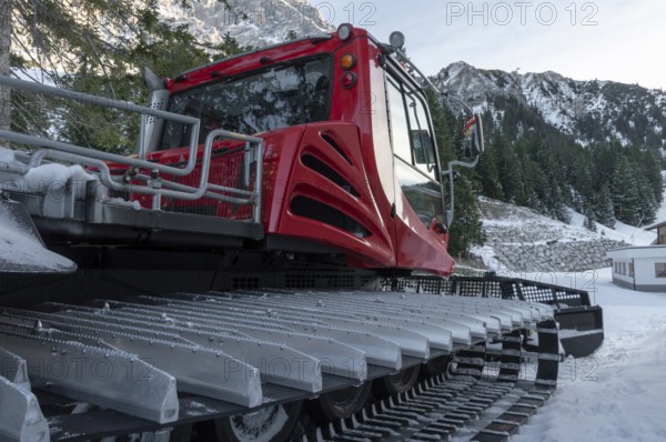 Tracked snow groomer with huge tracks in a winter scenery with the snowy austrian alps and forest in background