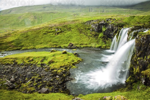 Overcast cold summer day in Iceland. Concept of extreme and exotic tourism. At the foot of the mountain Kirkjoufell powerful waterfalls Kirkjoufellfoss