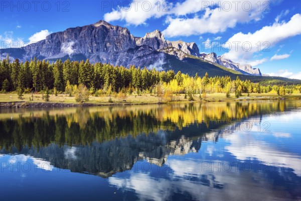 Concept hiking. Canmore, near Banff. Red-orange trees and jagged mountains are reflected in the lake