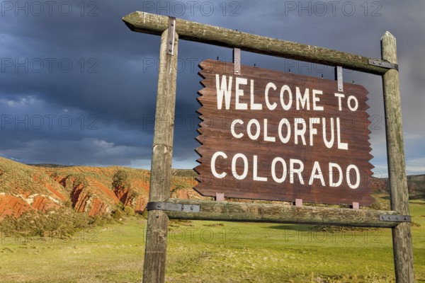 Welcome to colorful Colorado roadside wooden sign with red sandstone cliff in background