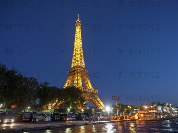 Eiffel Tower at night, illuminated, with its reflection in the water and people in the foreground, paris, france