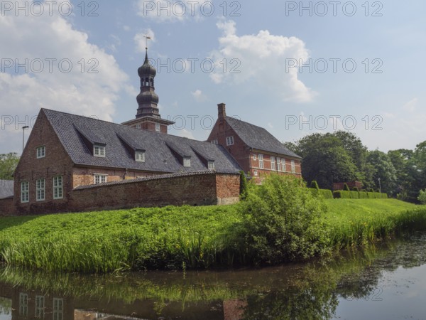 Historic brick building with tower and pond, surrounded by a green garden and blue sky, husum, schleswig-holstein, germany