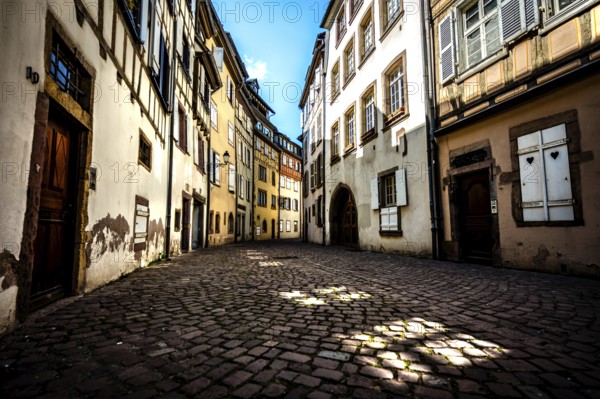Narrow alley in the old town of Colmar with cobblestones and historic buildings under a blue sky in Alsace, France