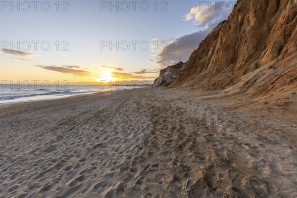 The golden sandy beach of Praia da Falésia with its characteristic orange-coloured cliffs, landscape shot in the evening at sunset on the cliffs in the Algarve, Portugal