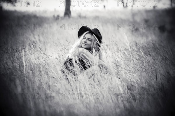 Young woman sitting in high grass in summertime in black and white